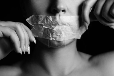 Foto de Mujer joven con la boca pegada sobre fondo oscuro, primer plano. Concepto de censura - Imagen libre de derechos
