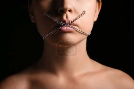 Young woman with chain on mouth against dark background. Censorship concept