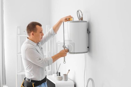 Photo for Male plumber repairing electric boiler in bathroom - Royalty Free Image