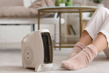 Calentador de ventilador eléctrico moderno y mujer en calcetines calientes en la alfombra, primer plano