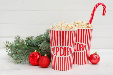 Eimer Popcorn mit Weihnachtskugeln und Tannenzweigen auf weißem Holzgrund