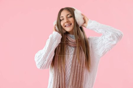Young woman in warm ear muffs and scarf on pink background