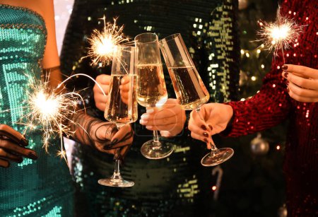 Photo for Young women in beautiful dresses with glasses of champagne and Christmas sparklers, closeup - Royalty Free Image
