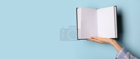 Hand holding blank book on light blue background with space for text