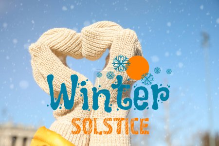 Woman in warm mittens making heart with her hands outdoors. Winter Solstice celebration