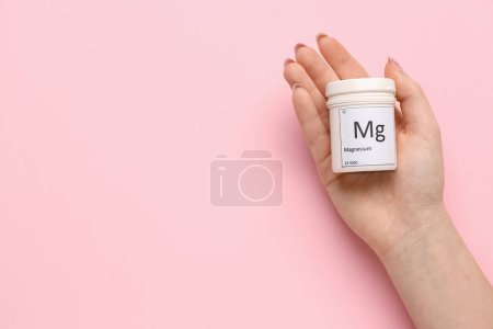 Foto de Mano femenina con frasco de píldoras de magnesio sobre fondo rosa, primer plano - Imagen libre de derechos