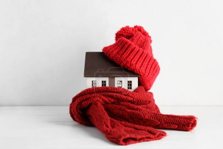 House model with hat and scarf on white wooden background. Heating concept