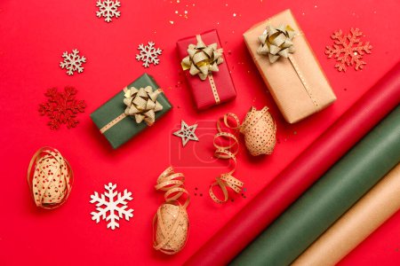 Téléchargez les photos : Composition avec cadeaux de Noël, décorations et matériaux d'emballage sur fond rouge - en image libre de droit