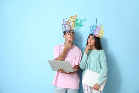 Téléchargez les photos : Jeune couple réfléchi avec de nombreuses flèches dans la tête et avec des ordinateurs portables sur fond bleu - en image libre de droit