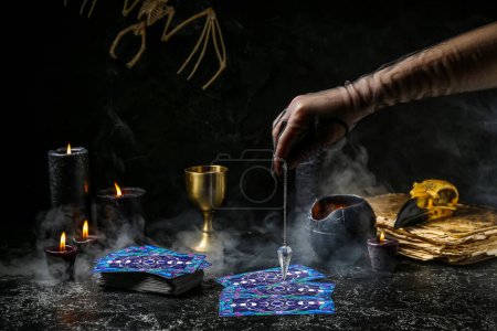 Photo for Fortune teller using pendulum and tarot cards to read future on dark background - Royalty Free Image