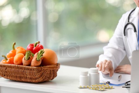 Photo for Female doctor with vitamins and vegetables sitting at table in clinic - Royalty Free Image