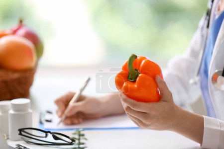 Photo for Female doctor with bell pepper writing in clipboard at hospital, closeup - Royalty Free Image