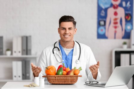 Männlicher Arzt mit Vitaminen und Gemüse sitzt in Klinik am Tisch