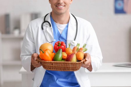 Photo for Male doctor holding basket with healthy food in clinic - Royalty Free Image
