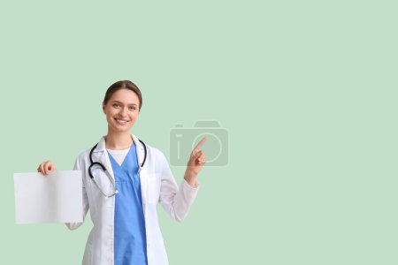 Photo for Female doctor with blank paper sheet pointing at something on green background - Royalty Free Image