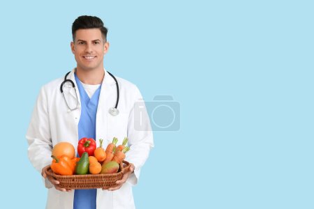 Male doctor holding basket with healthy food on blue background