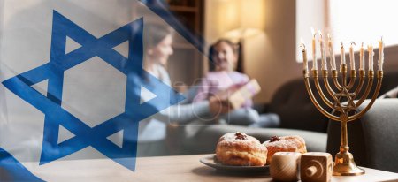 Foto de Bandera con bandera nacional israelí y menorah, dreidels y donuts en la mesa de la familia feliz celebrando Hannukah en casa - Imagen libre de derechos
