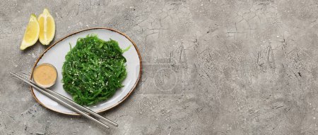 Téléchargez les photos : Assiette avec salade d'algues savoureuses et sauce sur fond grunge avec espace pour le texte - en image libre de droit