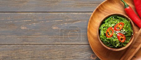 Téléchargez les photos : Bol avec salade d'algues saines et piment sur fond bois foncé avec espace pour texte - en image libre de droit