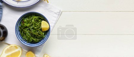 Téléchargez les photos : Bol avec salade d'algues saines et citron sur fond blanc en bois avec espace pour le texte - en image libre de droit