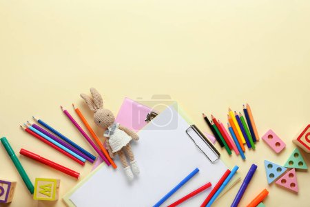 Clipboards with blank paper sheet, pencils, felt-tip pens and toy on beige background