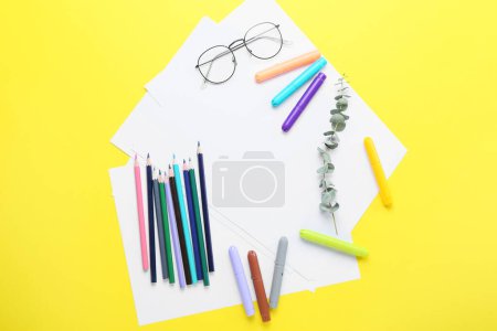 Téléchargez les photos : Feuilles de papier vierges avec lunettes, crayons, feutres, gommes et aiguiseurs sur fond jaune - en image libre de droit