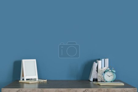 Photo for Frame with alarm clock, books and Christmas decor on table near blue wall - Royalty Free Image