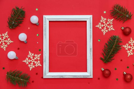 Foto de Composición con marco vacío, ramas de abeto y decoraciones navideñas sobre fondo rojo - Imagen libre de derechos