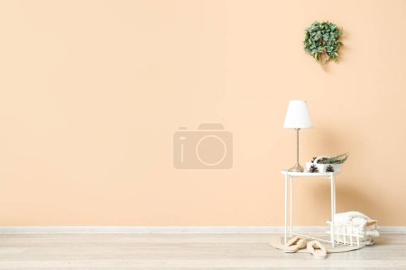 Photo for Table with lamp, slippers and Christmas mistletoe wreath on beige wall in room - Royalty Free Image