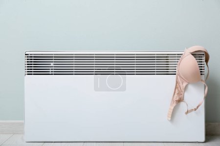 Foto de Sujetador femenino secado en radiador eléctrico cerca de pared de luz - Imagen libre de derechos