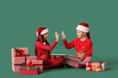 Foto de Niños pequeños en pijama con regalos de Navidad y libro que se dan choca los cinco sobre fondo verde - Imagen libre de derechos