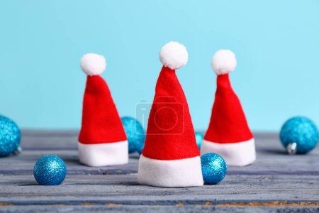 Foto de Sombreros de Santa y bolas de Navidad sobre mesa de madera oscura sobre fondo de color - Imagen libre de derechos