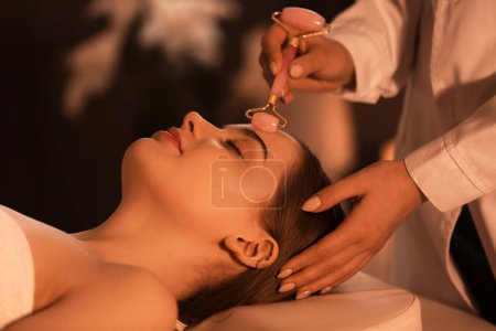 Photo for Pretty young woman receiving face massage with roller in beauty salon - Royalty Free Image
