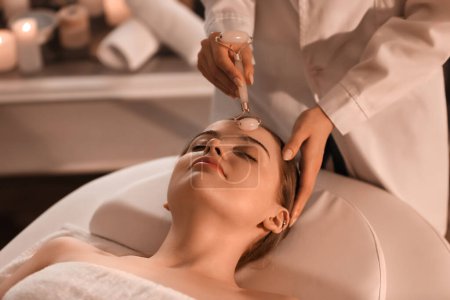 Photo for Pretty young woman receiving face massage with roller in beauty salon - Royalty Free Image