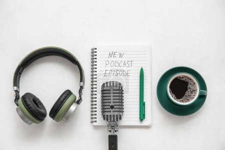Foto de Cuaderno con texto NEW PODCAST EPISODE, micrófono, taza de café y auriculares sobre fondo blanco - Imagen libre de derechos