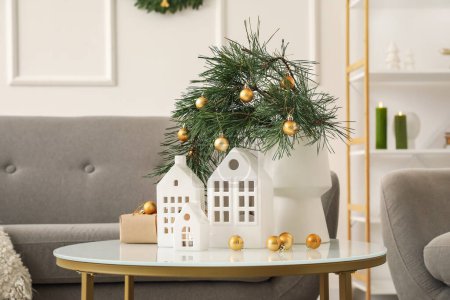 Téléchargez les photos : Vase avec branches de Noël, boules et bougeoirs en forme de maison sur la table dans le salon - en image libre de droit