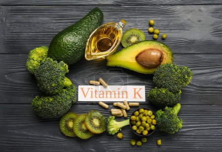 Composition with text VITAMIN K, pills and healthy products on black wooden background