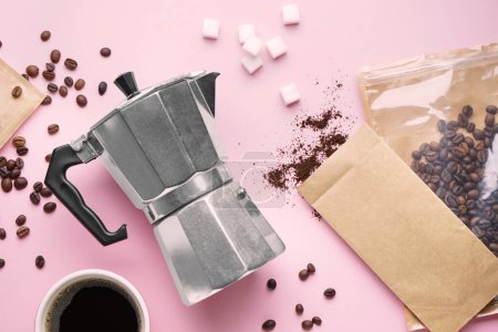 Foto de Cafetera géiser, taza de espresso, azúcar y bolsas con frijoles sobre fondo rosa - Imagen libre de derechos