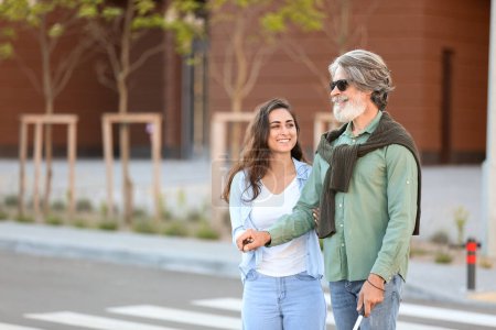 Téléchargez les photos : Une jeune femme aide un aveugle âgé à traverser la route en ville - en image libre de droit