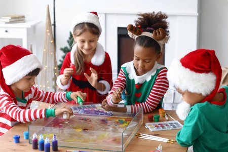 Téléchargez les photos : Petits enfants en costumes de Noël versant des peintures dans l'eau à l'atelier de peinture Ebru - en image libre de droit