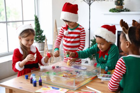Téléchargez les photos : Petits enfants en costumes de Noël versant des peintures dans l'eau à l'atelier de peinture Ebru - en image libre de droit