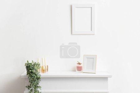 Téléchargez les photos : Cadre photo vierge, bougies et plantes d'intérieur sur cheminée près du mur blanc - en image libre de droit