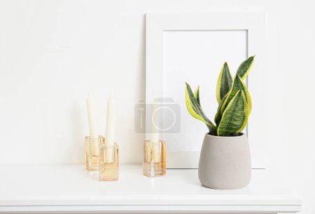 Téléchargez les photos : Plante d'intérieur, cadre photo vierge et bougies sur l'étagère près du mur blanc - en image libre de droit