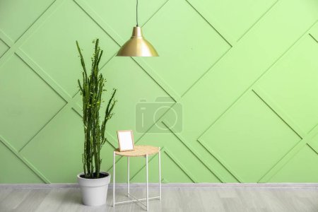 Foto de Mesa con marco de fotos en blanco y cactus cerca de la pared verde en la habitación - Imagen libre de derechos