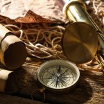Compass with spyglass and maps on dark wooden background