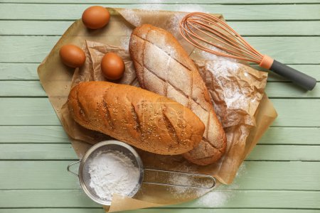 Photo for Baking paper with loafs of fresh bread, eggs and flour on color wooden background - Royalty Free Image