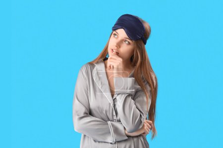 Photo for Young woman in pajamas biting nails on blue background - Royalty Free Image