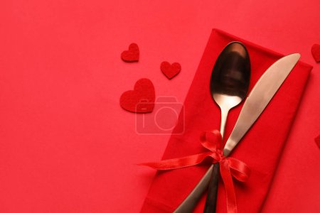 Cutlery with bow and hearts on red background. Valentine's Day celebration