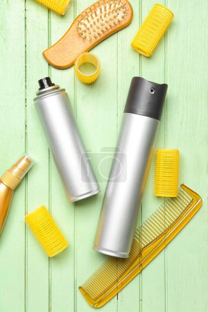 Hair sprays with curlers and combs on green wooden background