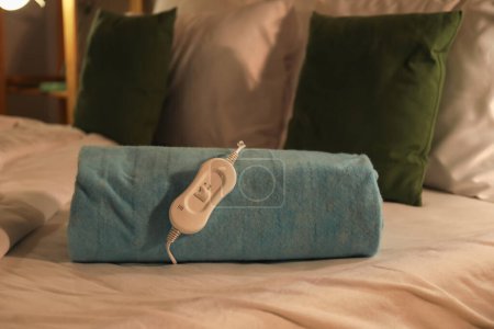 Foto de Almohadilla eléctrica plegable con controlador en la cama por la noche, primer plano - Imagen libre de derechos